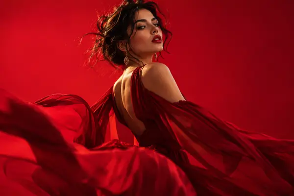 A fashion performer poses confidently against a vivid red studio backdrop.