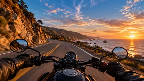 A motorcycle rider's view down an empty coastal road beneath a broad blue evening sky.